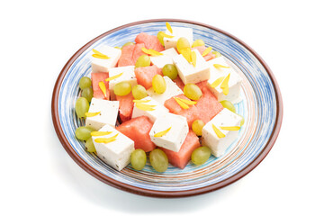 Vegetarian salad with watermelon, feta cheese, and grapes on blue ceramic plate isolated on white background. Side view