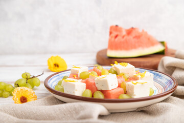 Vegetarian salad with watermelon, feta cheese, and grapes on blue ceramic plate on white wooden background. Side view, selective focus.