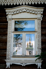 Reflection of a church in Konstantinovo in the window of a wooden house