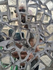 Close-up of a wall with broken mirrors and a reflection of a human figure behind.