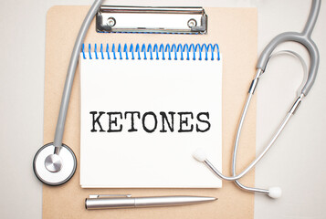 White notepad with the words ketones and a stethoscope on a blue background. Medical concept