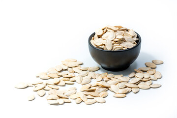 Pumpkin seeds in a bowl isolated on white background with some seeds spilled around. Roasted and salted pumpkin seeds for snacks