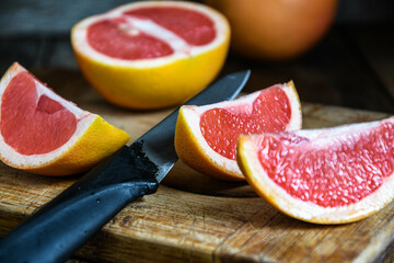 Sliced grapefruit with a knife on a cutting board in the kitchen on a wooden table.