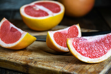 Sliced grapefruit with a knife on a cutting board in the kitchen on a wooden table.