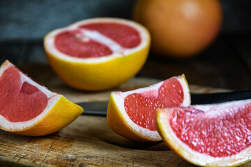 Sliced grapefruit with a knife on a cutting board in the kitchen on a wooden table.