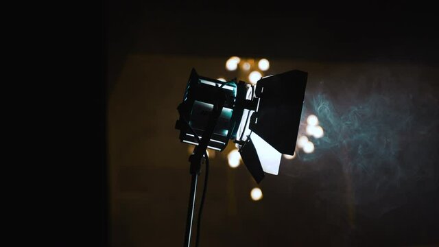 Bright light on a tripod. Professional light for photo and video shooting. Spotlight in a dark room. The lantern illuminates the smoke that rises.