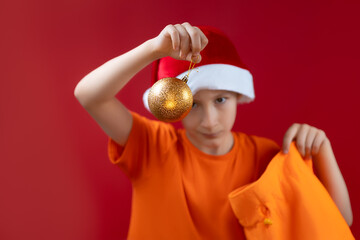 A boy in a Santa Christmas hat holds a gift bag with Christmas toys pulled out of it by a Christmas toy