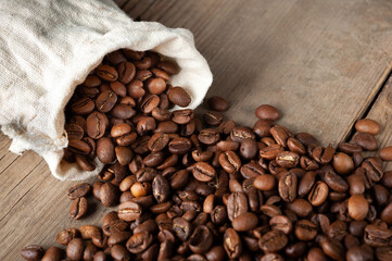 coffee beans are falling from a white sack on an old wooden background. Copy space