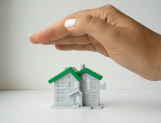 Figure of a toy house covered with a hand on a white background. Property insurance concept