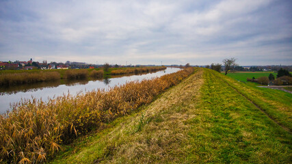 Blick entlang des Elster-Saale-Kanals mit herbstlichem Schilfufer und Deich unter bew&ouml;lktem Himmel, Leipzig, Sachsen, Deutschland