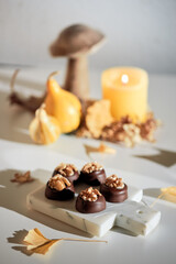 Chocolate pralines with walnut nuts on marble cutting board. Closeup on candy. Autumn arrangement with candle, pumpkins, wooden mushroom anddry yellow ginkgo leaves. Natural sunlight, with long