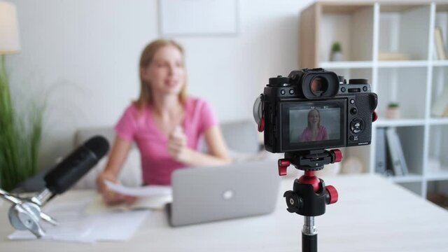 Educational blog. Female speaker. Video recording. Inspired woman giving important information on photo camera in light home studio interior.