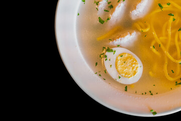 Dietary soup with chicken meatballs, egg and noodles in white plate isolated on a black background. Pasta. Greens. Flavouring