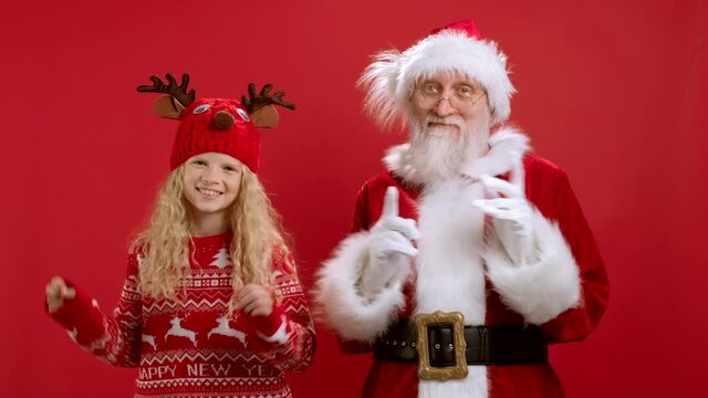 Happy Cheerful Santa Claus and Blonde Teenage Girl are Having fun Dancing Together to Christmas Music and Catching Gift Boxes on Red Background in Their Hands. New Year and Christmas Gifts.