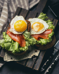 Sandwich toasts with egg,smoked salmon and lettuce on brown bread on textured wooden cutting board