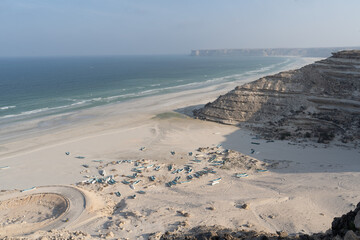 Majestic Coastal Cliffs. Imposing cliffs stand guard by the serene beaches of southern Oman,...