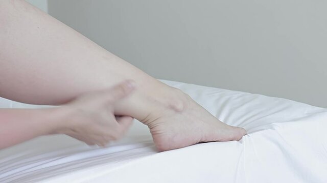 Woman doing legs and foot self massage in bed, she massaging ligaments and calves, relief for tired legs and feet, body care and treatment at home