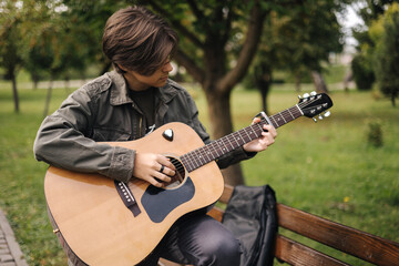 Handsome teenage playing acoustic guitar with capo. Boy sitting on bench and playing music