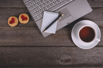 Overhead view of modern workspace with laptop,notebook and pen,a cup of tea and some biscuits