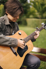 Fototapeta premium Handsome teenage playing acoustic guitar with capo. Boy sitting on bench and playing music