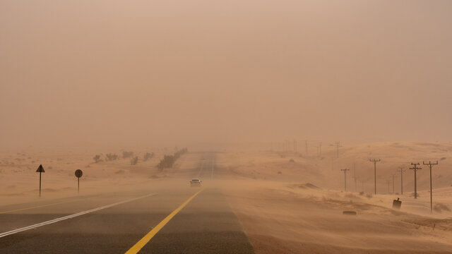 Sandstorm in the Saudi Desert with a lone car driving on the road