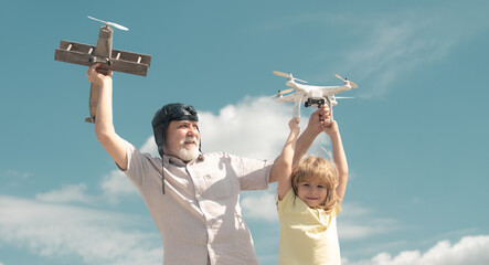 Old grandfather and young child grandson playing with toy plane and quadcopter drone against sky. Child pilot aviator with plane dreams of traveling.