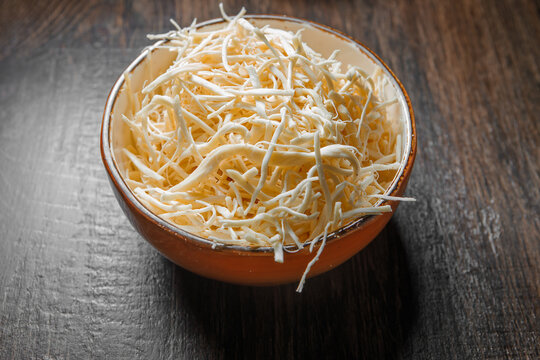 Fibrous chechil cheese in a deep cup stands on a wooden table.