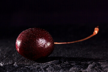 one red cherry with water drops on a black stone background