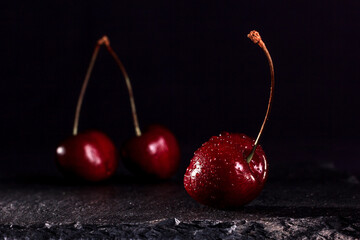red cherries with water drops on black stone stand on a black background
