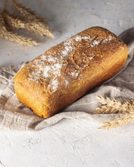 Whole grain loaf bread sprinkled with flour and spikelets of rye isolated on white background