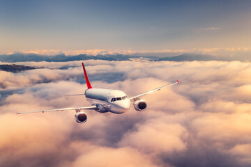 Naklejka na ściany i meble Airplane is flying above the clouds at sunset in summer. Landscape with passenger airplane, beautiful clouds, mountains, sky. Aircraft is taking off. Business travel. Commercial plane. Transport