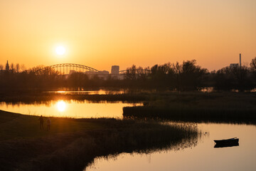 Fototapeta premium Setting sun behind the bridge over the Waal (Rhine) river in Nijmegen against an orange evening sky