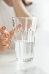 Close-up of a glass half filled with clean water. The child wants to take a glass and have a drink. Mineral water. Vertical photo