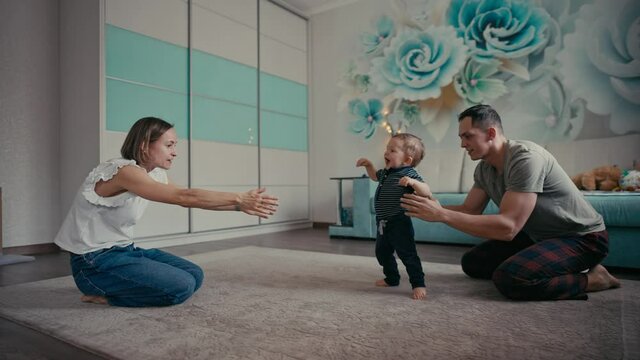 Happy family smiling as baby takes first steps. Family At Home Encouraging Baby Son To Take First Steps.