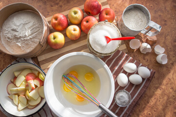 Eggs hammered into a white bowl for a delicious and airy sponge cake with apples.