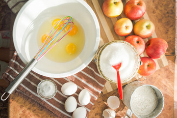 Eggs hammered into a white bowl for a delicious and airy sponge cake with apples.