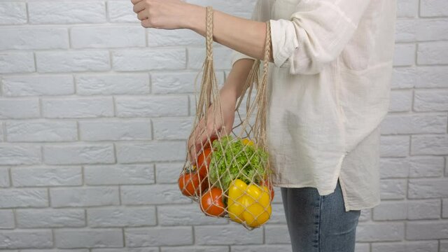 Vegetables in a net. A woman hold a string bag with ripe vegetables in the room.