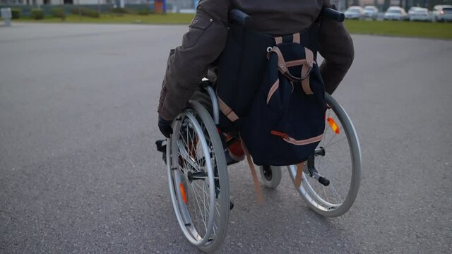 alone disabled man in wheelchair is moving independently on city street, rear view