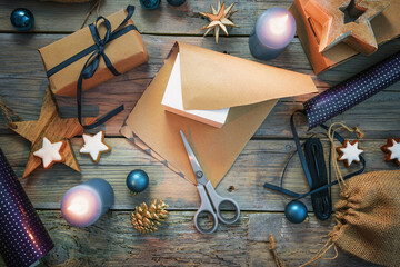 Fototapeta na wymiar Wrapping gifts with natural brown paper and blue ribbon, Christmas decoration like balls, stars and lit candles on a rustic wooden table, flat lay, high angle view from above