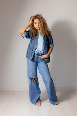 young curly haired woman with blue eyes in a full length denim suit. model poses in the studio. space for text. High quality photo