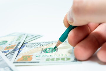 Draw money. A bang in hand holds a pencil over a hundred dollar bill.