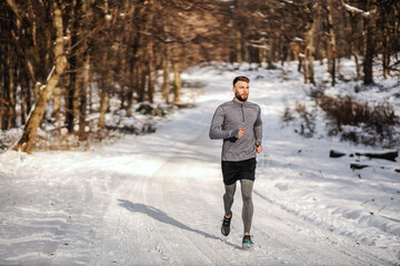 Fit sportsman running in forest at sunny snowy winter day. Outdoor fitness, cardio exercises, winter fitness