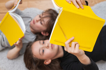 Young girl with her little brother enjoying reading together from yellow book.