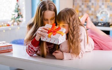 two girls are sitting in the kitchen and shaking boxes with gifts