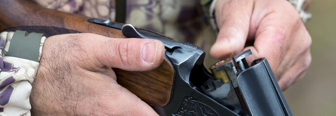 Fototapeta premium Charges a hunting smooth-bore rifle, hunting a pheasant with dogs. A hunter in camouflage is standing with a weapon.