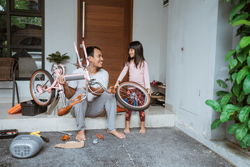 Father holding bicycle frame and daughter carrying wheels