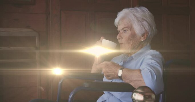 Animation of light moving over senior caucasian woman in wheelchair drinking coffee