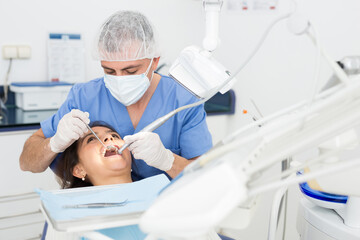 Man dentist holding dental drill and treating teeth of girl in dentist office