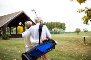 Senior couple with golf equipment hugging each other and looking far away on the golf course.