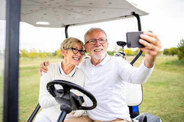 Portrait of healthy senior couple taking a selfie photo in golf car before the training.
